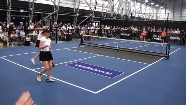 The same pickleball rally with a condados.ai banner lying flat on the near court, staying fixed to the floor while the players move over it